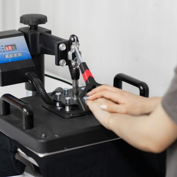 Person operating a heat press machine to apply a heat transfer design to black fabric.