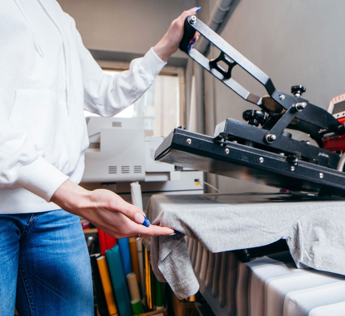Person using a heat press machine to apply a design to a grey T-shirt.