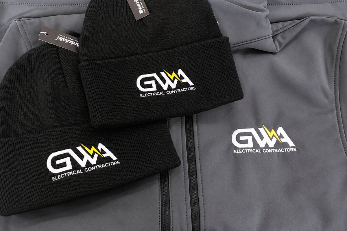 Black beanie hats and grey workwear jackets embroidered with the GWA Electrical Contractors logo.